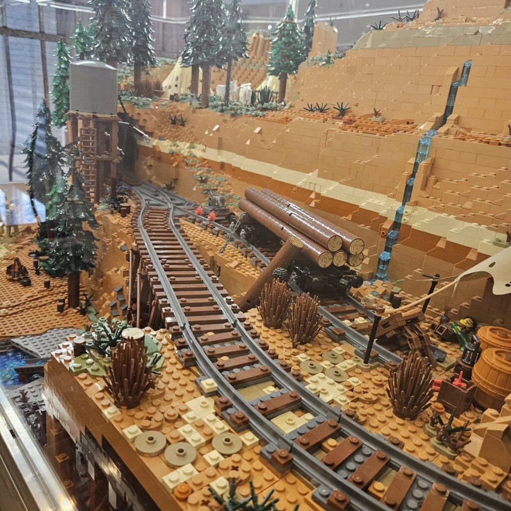LEGO diorama of a desert canyon with railroad tracks winding through brown and tan bricks and scattered trees and vegetation